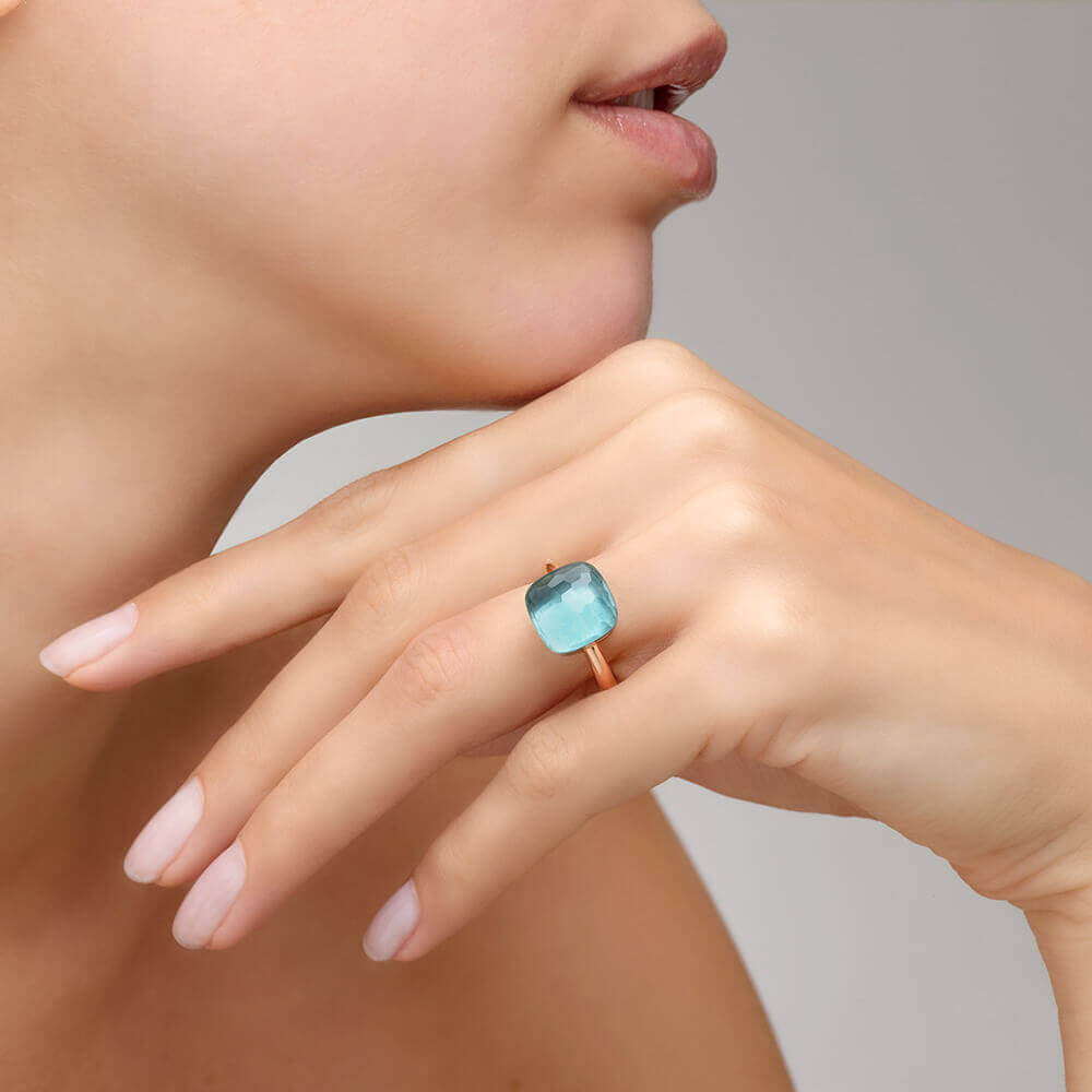 Ring Nudo Maxi aus 750er Roségold mit Weißgold-Einfassung und hellblauem Topas, an einer Hand getragen.